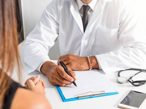 A doctor takes notes while discussing diagnosis with patient; his notes will be available for patient to view securely online.