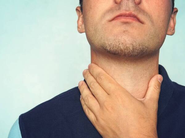 A young man grabs his neck to check for symptoms of thyroid disease.