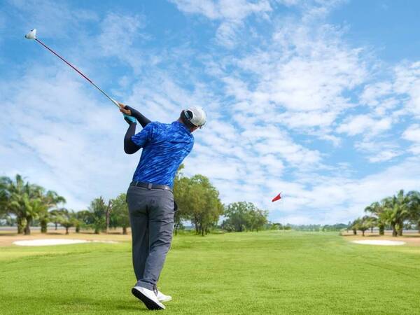 A male golfer swings away on an open green golf course, showing proper form that will prevent joint problems.
