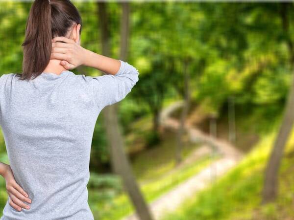 The back of a woman holding her neck, trying to relieve her neck pain.