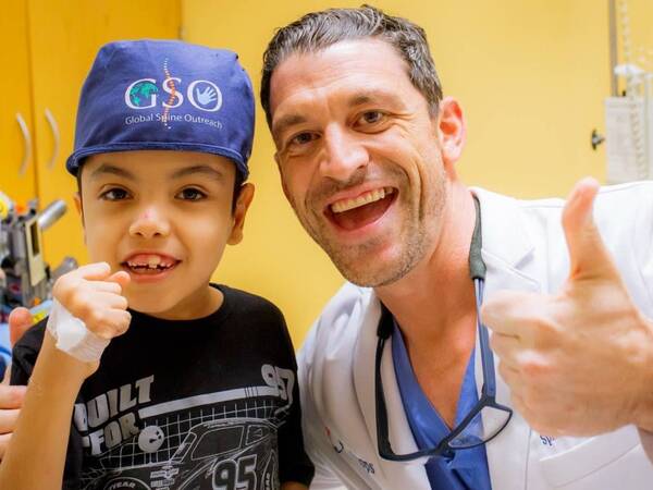 Gregory Mundis, MD, a spine surgeon, and a child patient give the thumbs up sign after a successful spine surgery.