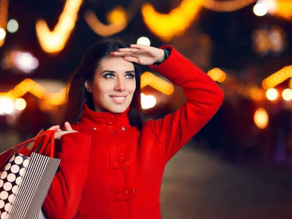 A woman is smiling while shopping for Christmas gifts, her way of dealing with holiday stress.