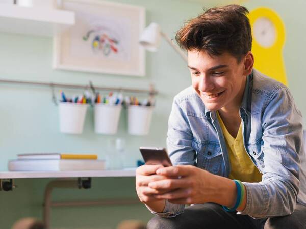 A young man looking at his cell phone demonstrates the need for screen time limits, as studies show people spend hours a day staring at electronic devices.