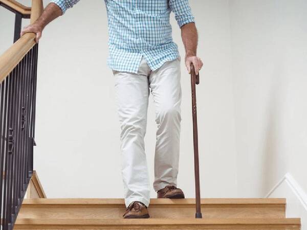 An elderly man uses handrails to walk down stairs with aid of cane.