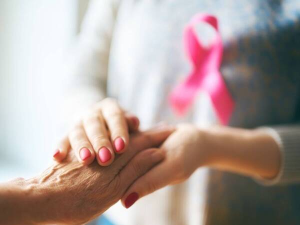 Inflammatory breast cancer patient holds hand of supporter with cancer ribbon in background.