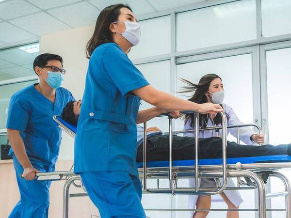 A trauma team rushes a patient in a gurney down a hospital hallway. 