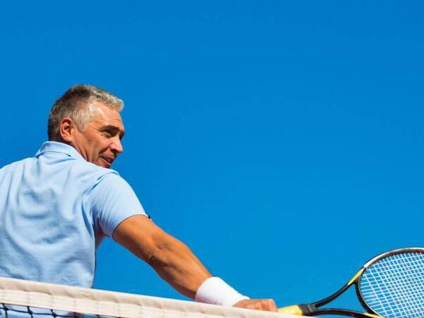 An older man with gray hair hits a tennis ball over the net.