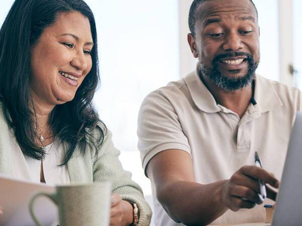 A man and a woman smile as they look at the computer while comparing health insurance plans in preparation for open enrollment.