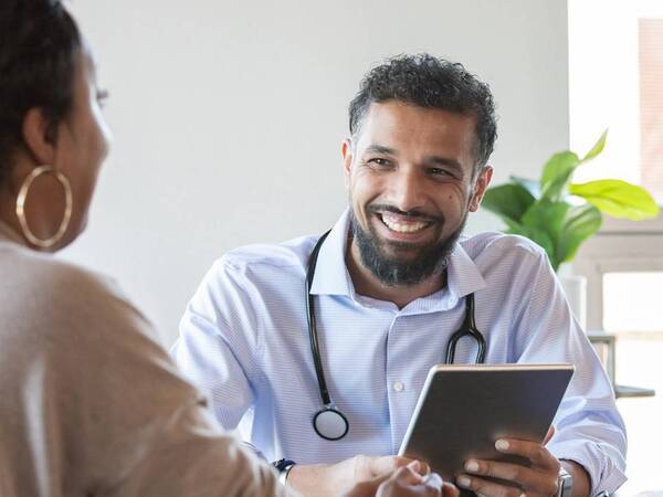 A young, male primary care physician smiles as he talks with a patient. 