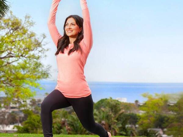 Kosha Nathwani, MD, a family medicine physician at Scripps Clinic Encinitas, is in a warrior 1 yoga pose outdoors with the ocean in the background. - San Diego Health Magazine