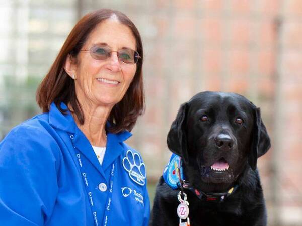 A canine therapy volunteer and her dog smile outside the hospital.