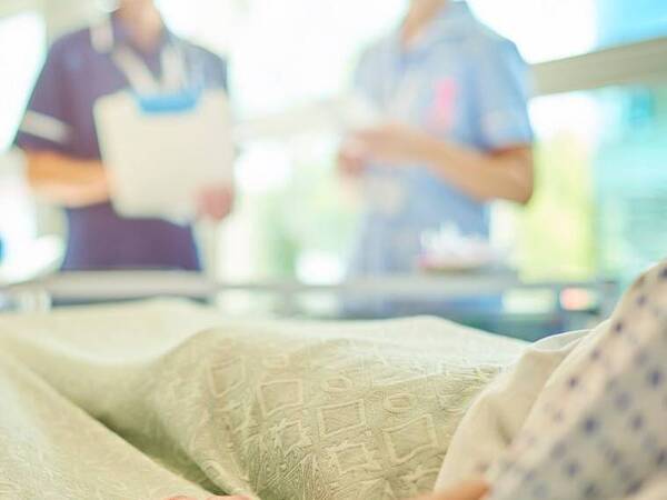 Hospital staff members check on a patient in a hospital bed.