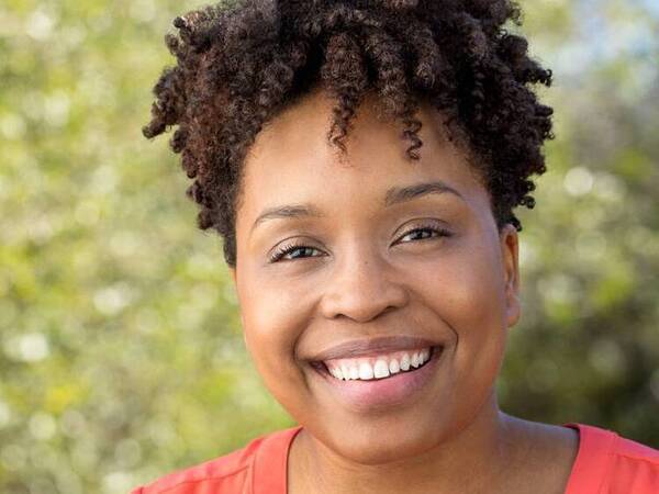 A young black woman smiles in an outdoor setting.