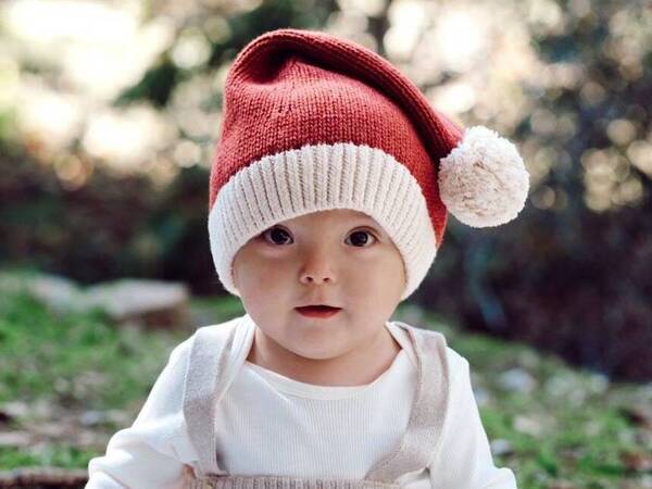 Baby Leo Dakin celebrates his first Christmas at home. He wears a Santa hat sitting outdoors on the grass in his family's backyard.