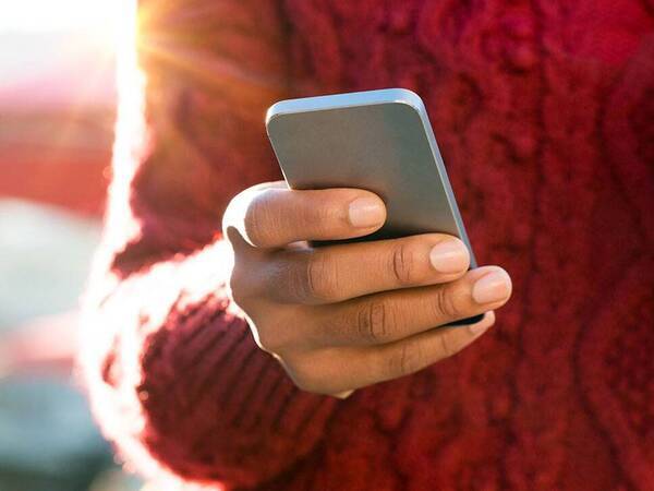 A person outside while the sun is shining and holding their smartphone.