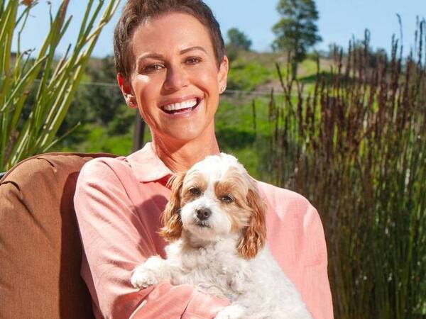 Kelly O'Connor smiles at home outdoors holding her small dog after breast cancer treatment.