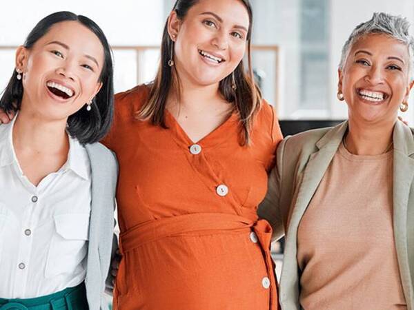 Four women of diverse backgrounds and ages smile together.