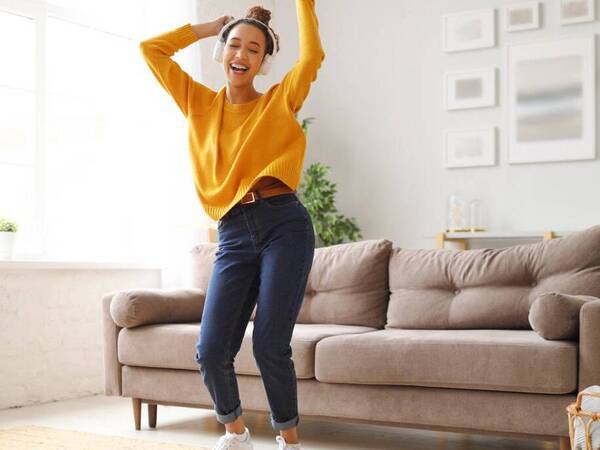 A young woman dances in her living room with headphones on.