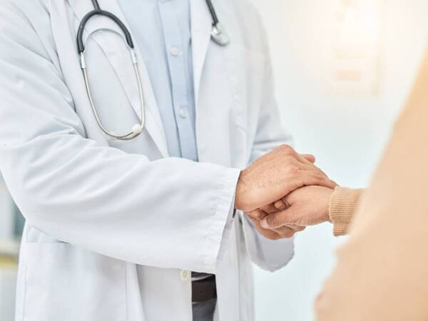 A radiation oncologist holds the hand of a cancer patient.
