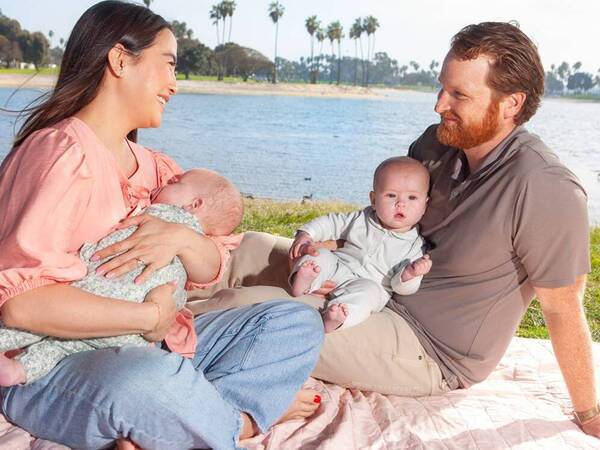 Caitlin Welsh and her husband, Kevin, smile as they sit on a blanket by the bay each holding one of their twin babies.