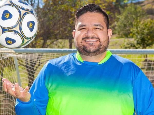 Juan Ramos tosses a soccer ball in his hand in front of a soccer goal post.