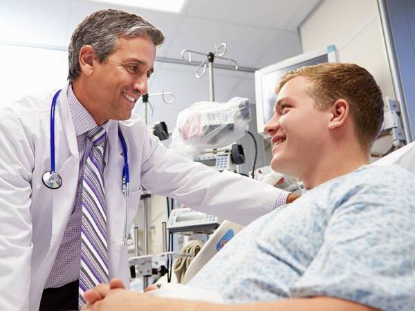 A patient in a hospital bed smiles as he talks to a doctor.