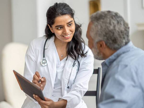 A  kind young female provider speaking and documenting their conversation with a male patient in a clinical setting.