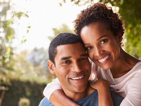 A smiling middle-aged woman and man cuddle close to each other, representing the enhanced appearance and confidence after facelift, rhinoplasty or otoplasty.
