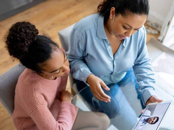 A mother viewing a video visit with her daughter and her daughter's provider as they sit in a home office.
