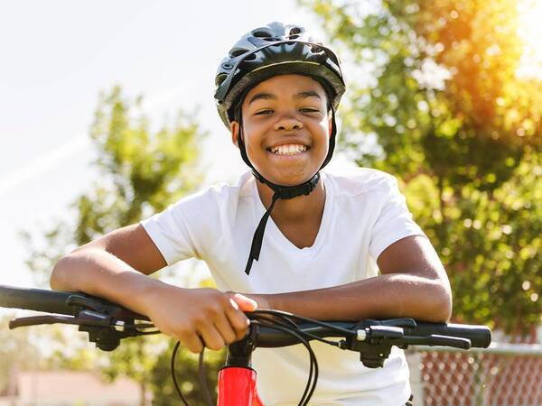 A young black male smiles as he sits on an ebike wearing a helmet for safety.