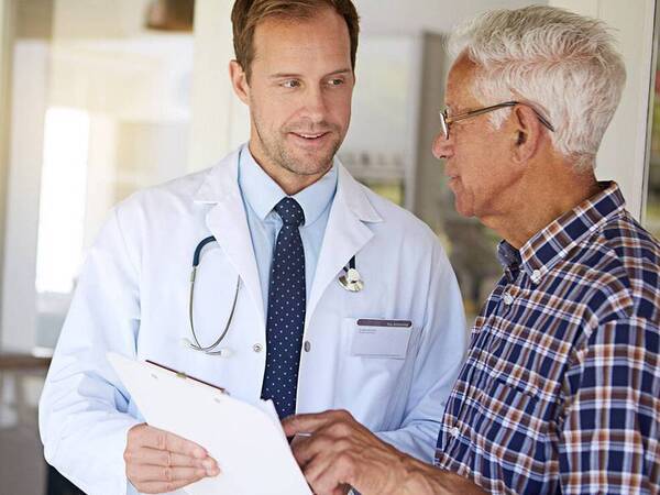 A male doctor speaking with an older male patient about cancer therapy options, including immunotherapy.