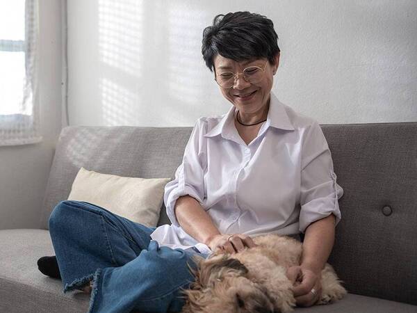 A woman sitting on her couch, smiling at her dog.