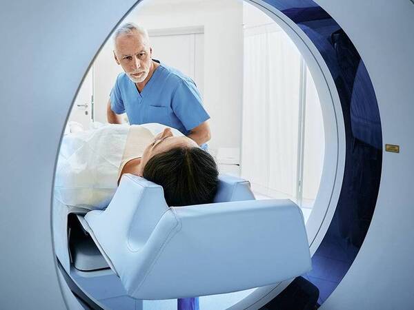 Patient in a CT machine with a provider near her, illustrating theronostics cancer treatment.
