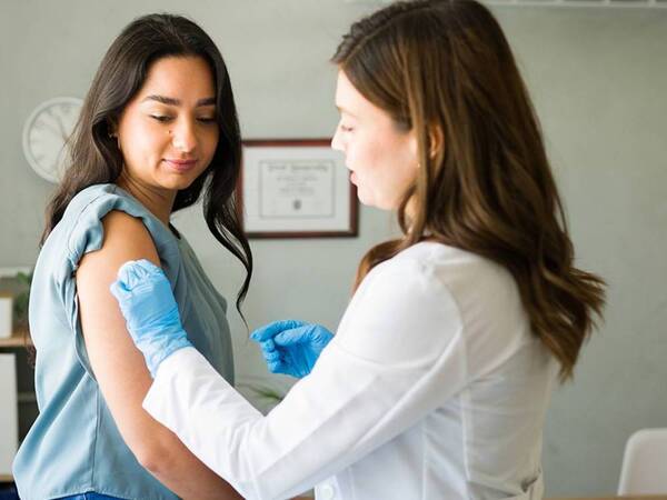 A young woman in her 20s is receiving her annual flu vaccination from a female provider.