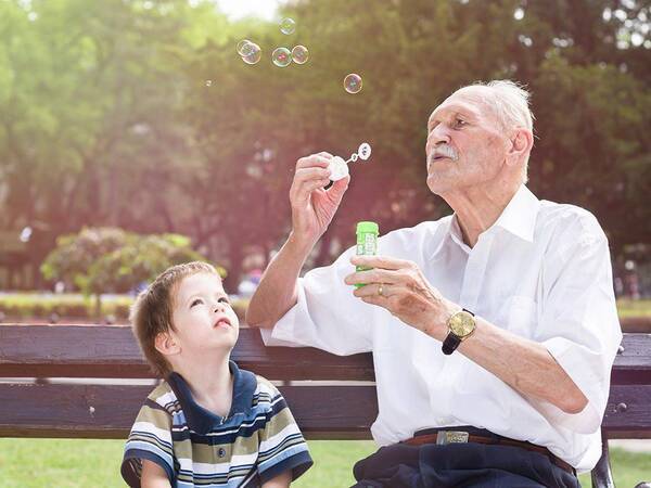 A mature man blows bubbles with his grandson on a park bench, representing the importance of stroke prevention.
