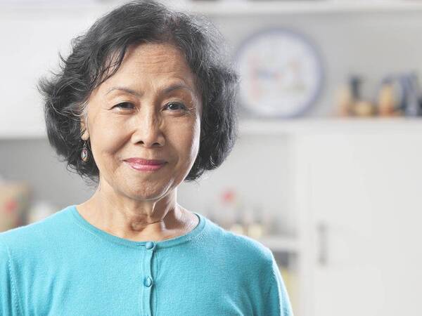 A smiling mature woman in her kitchen represents the importance of knowing the signs and symptoms of stroke.