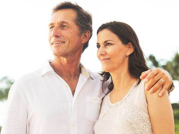A smiling middle-aged Caucasian couple on the beach represents the confidence you can have in cancer screening at Scripps.