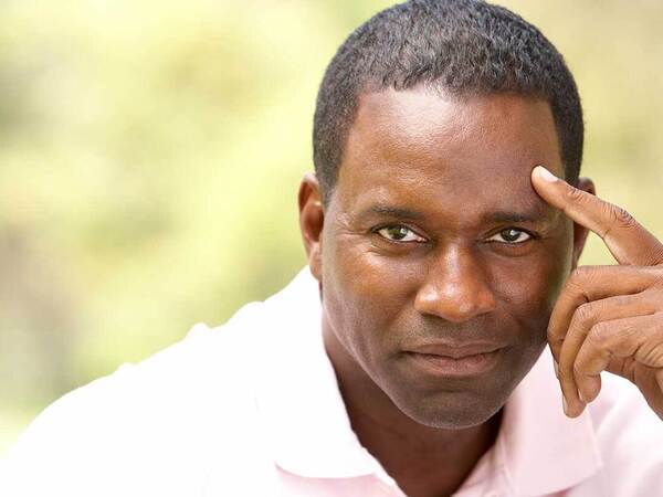 Middle-aged man thinks with fingers against his forehead.