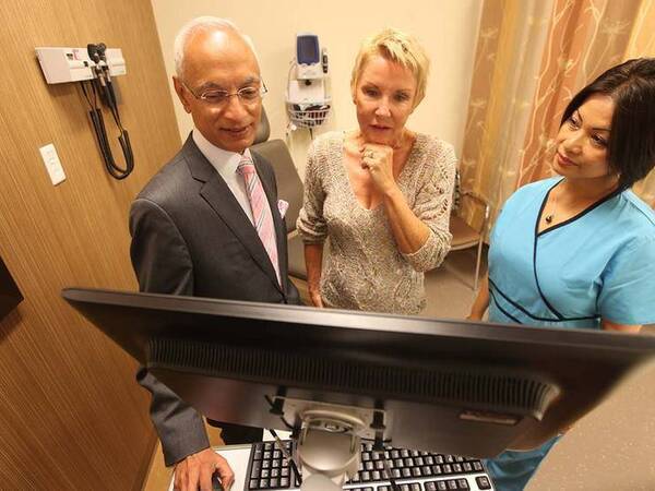 A Scripps radiation oncologist and nurse talk with a mature Caucasian woman in a patient exam room, representing the help patients get in understanding the different types of radiation therapy.