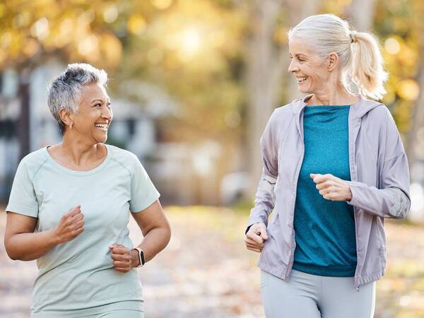 Two senior women smile as they walk outdoors representing successful rheumatology treatments. 