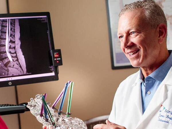 Dr. Bruffey holding a model in this hands while speaking with a patient about her diagnosis, illustrating orthopedic patient care a Scripps Health.