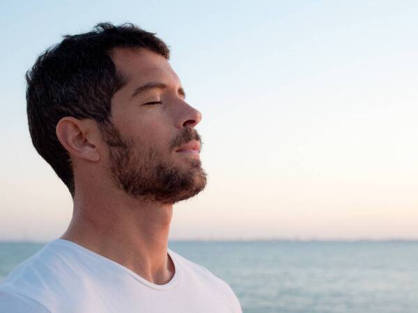A man takes a deep breath on the beach, representing an improved quality of life with expert care for blood disorders.