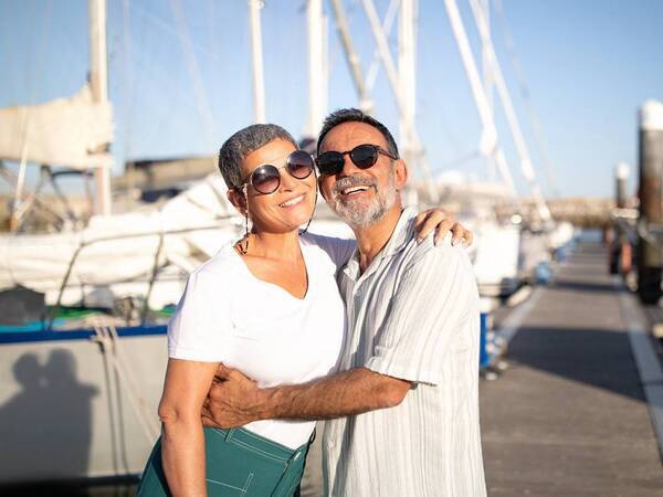 A middle-aged couple smiles at a boat dock.