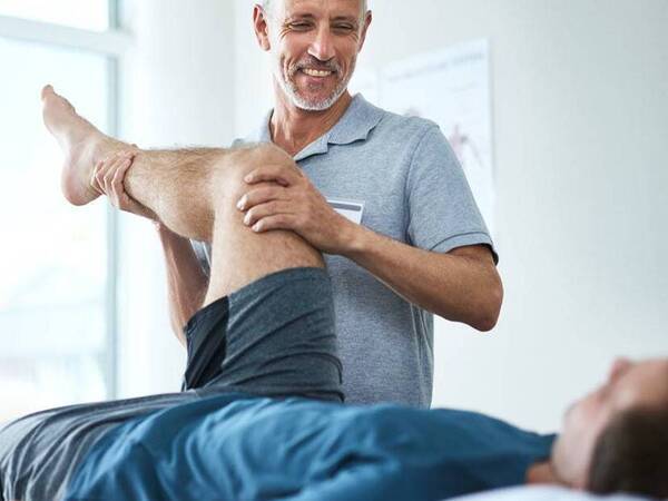 A physical therapy expert provides care to a reclining patient stretching his leg in a clinical setting.