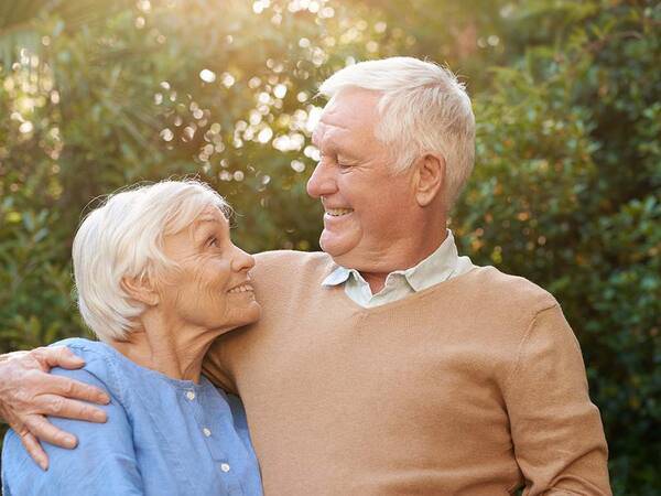 A smiling mature man and woman in their yard represent the improved quality of life with ALS treatment.