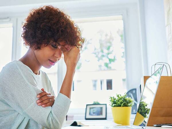 A middle-aged woman pinches the bridge of her nose, representing how headache and migraine pain can interrupt your life.