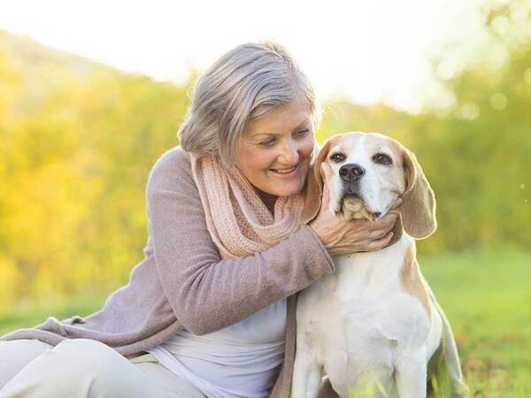 A smiling mature woman plays with her dog outdoors, representing the full life that can be led after anal cancer treatment.