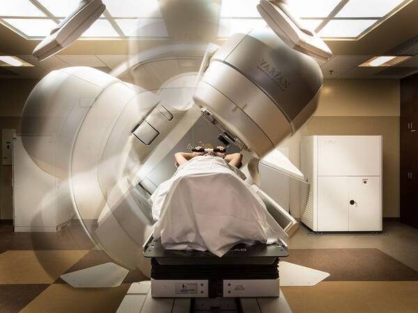 A patient comfortably lies down inside a rotating machine delivering external beam radiation therapy.