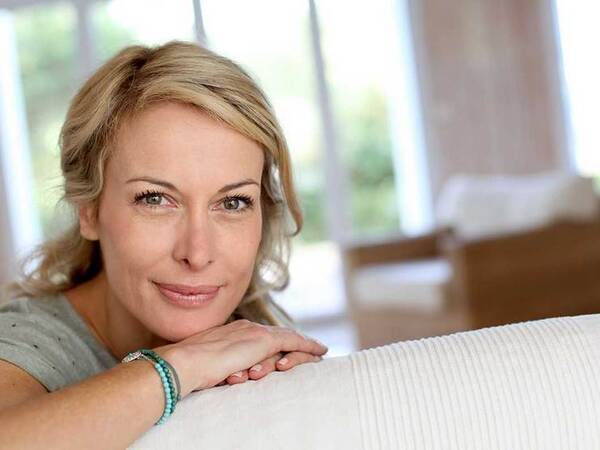 Smiling middle-aged woman looking over the back of a couch.