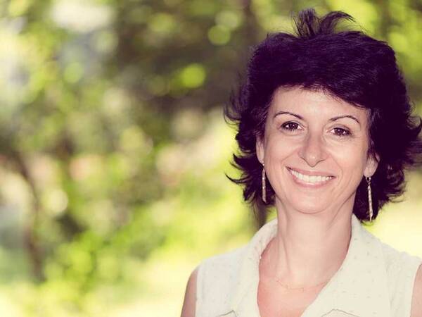 A smiling middle-aged woman in a park represents the full life that can be led after vulvar cancer treatment.